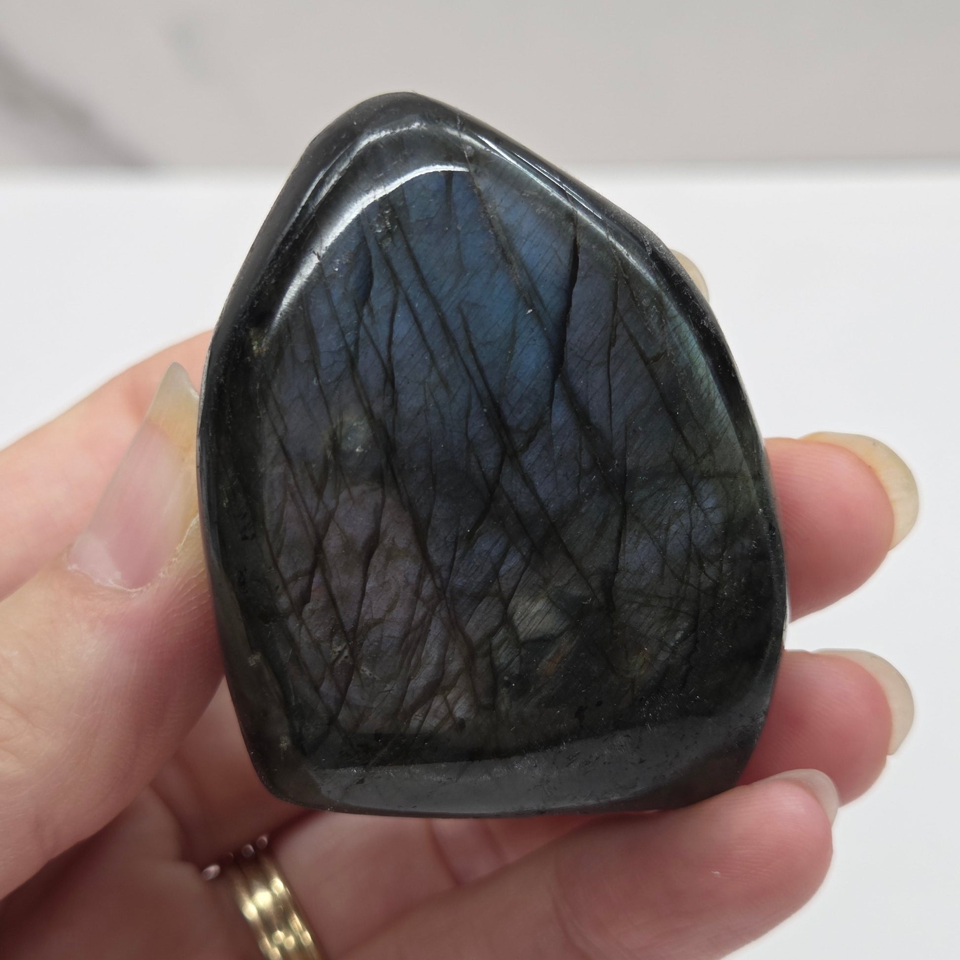 A polished Labradorite free form specimen being held by a hand showcasing a play of colors including blue, green, yellow, orange, red, and purple.
