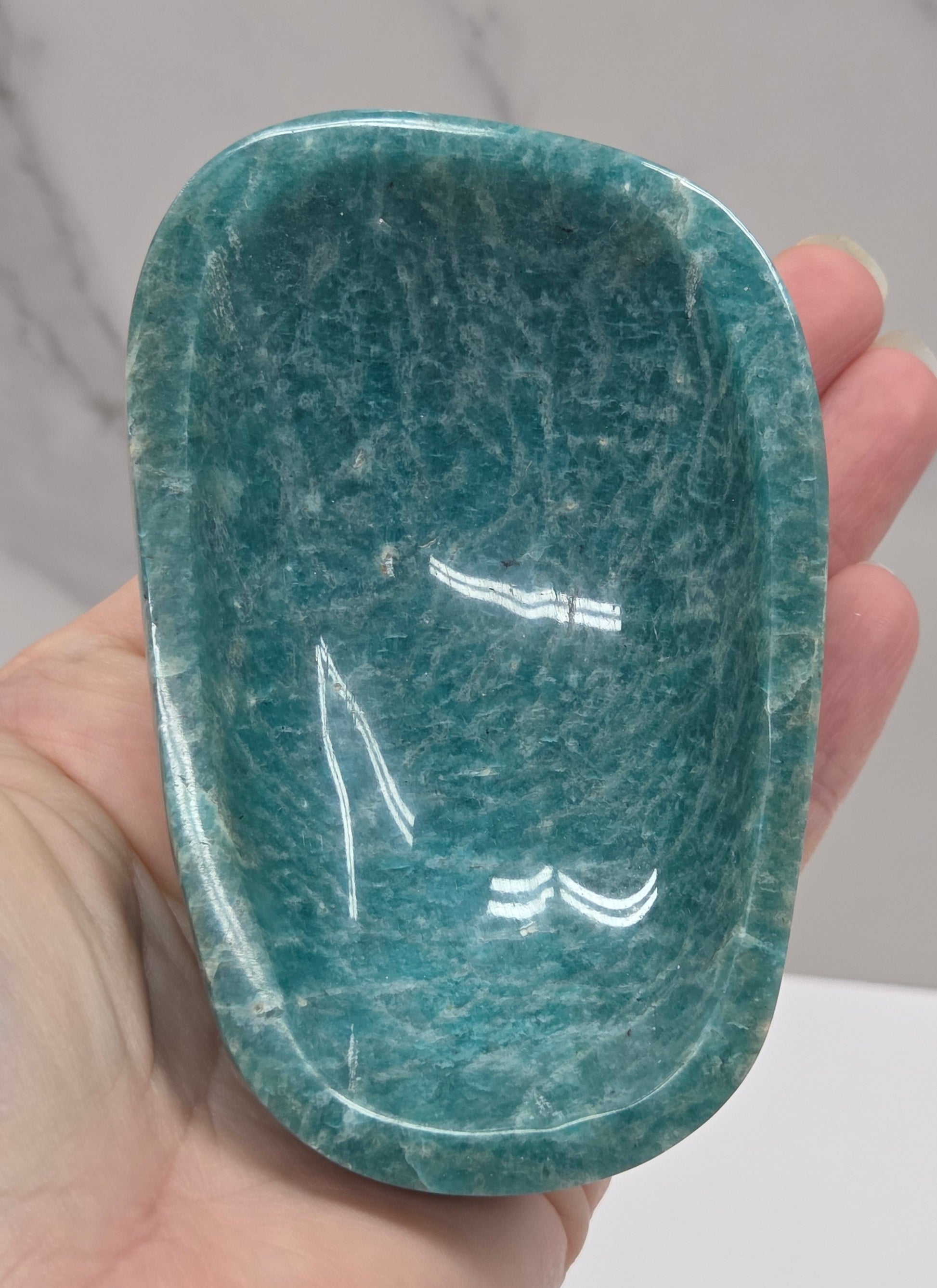 Hand holding a green amazonite carved bowls on a white background