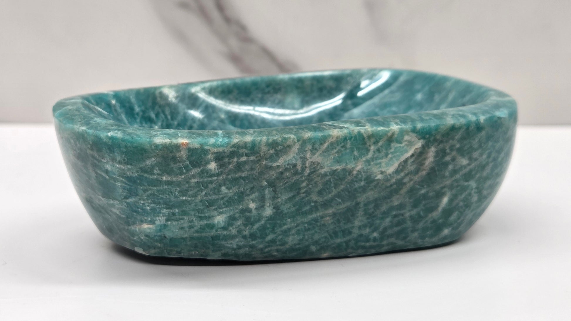 Green amazonite stone bowl on a white surface with a gray background