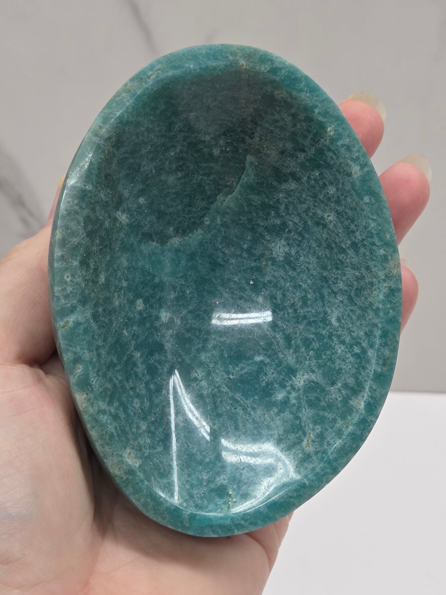 Hand holding a green amazonite carved bowls on a white background