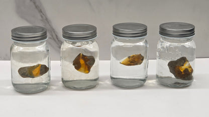 Four glass jars with metal lids containing opals on a marble surface.