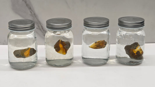 Four glass jars with metal lids containing opals on a marble surface.