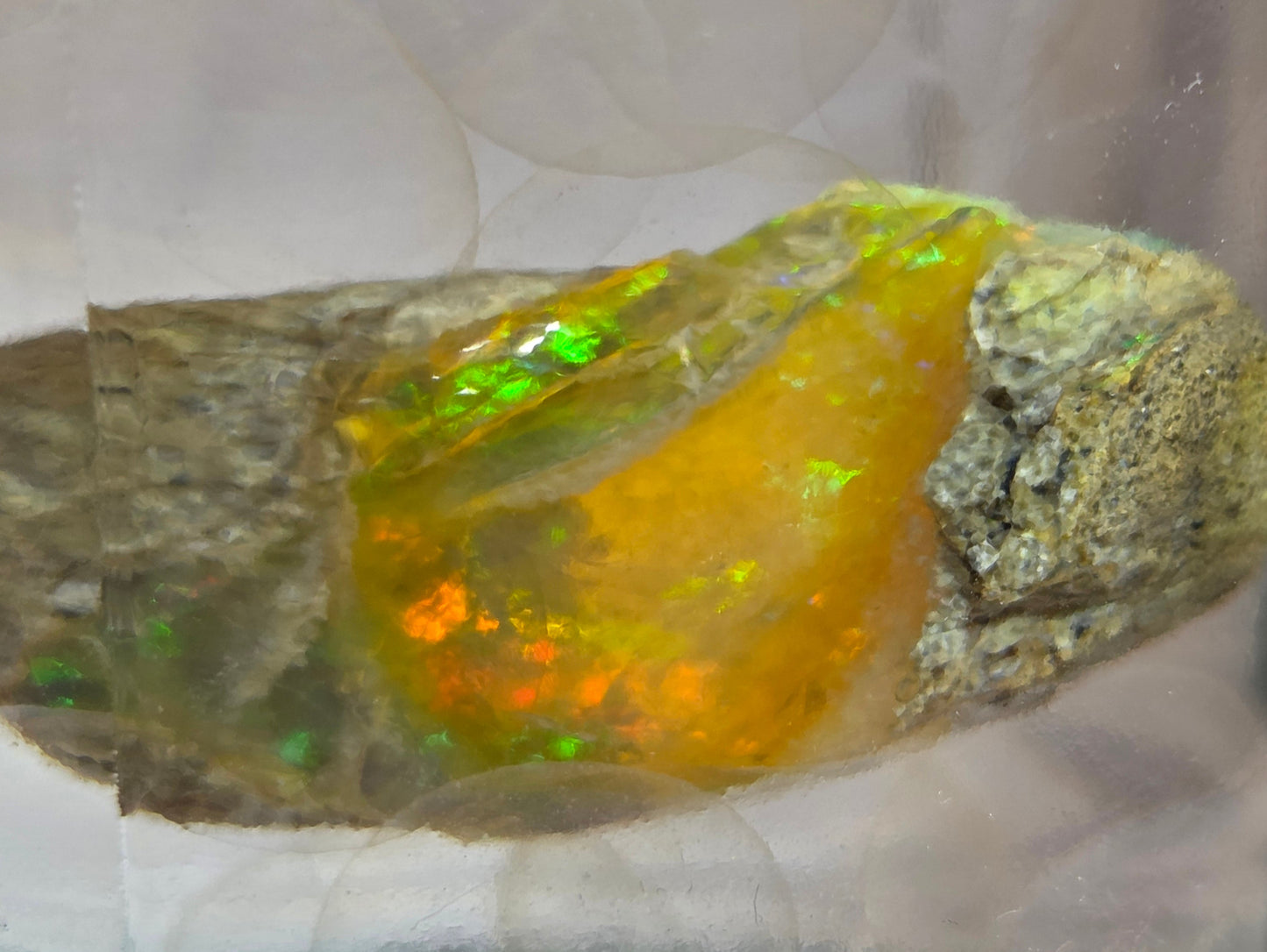 Mineral sample with a central yellow-orange crystal on a reflective surface
