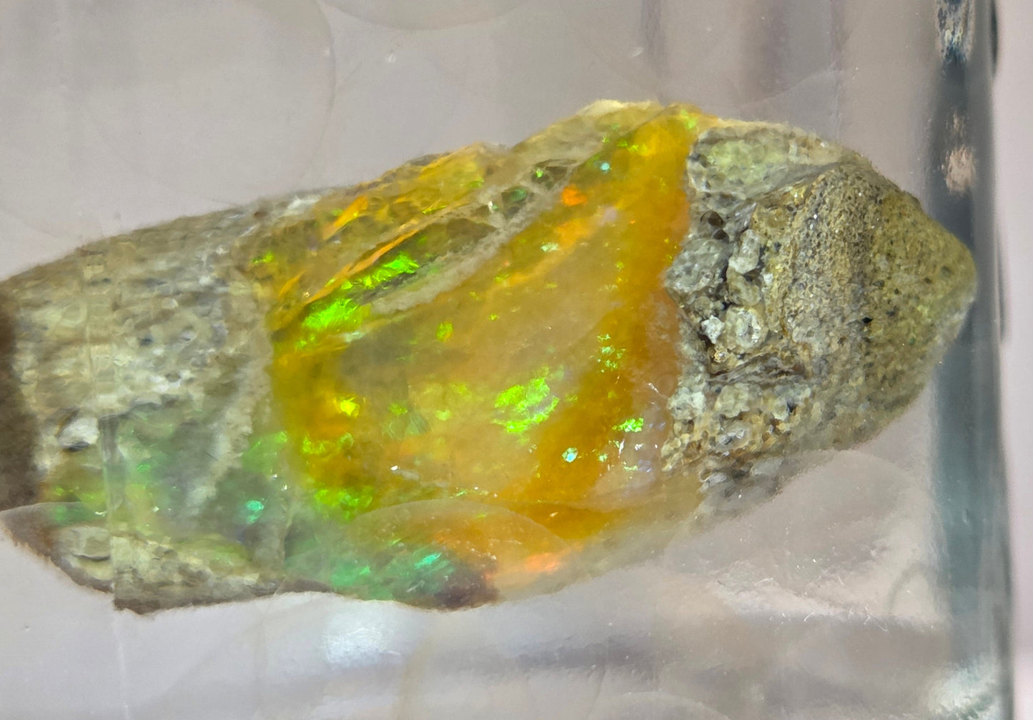Mineral sample with a central yellowish-orange crystal on a reflective surface