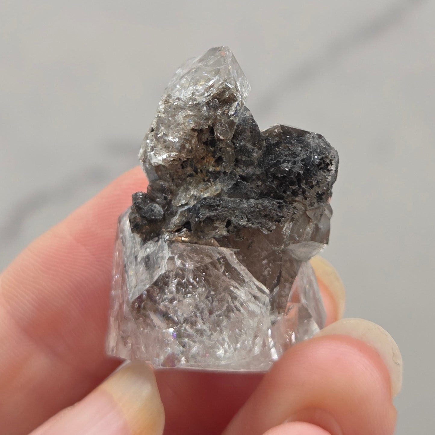 Hand holding a rough diamond crystal against a neutral background