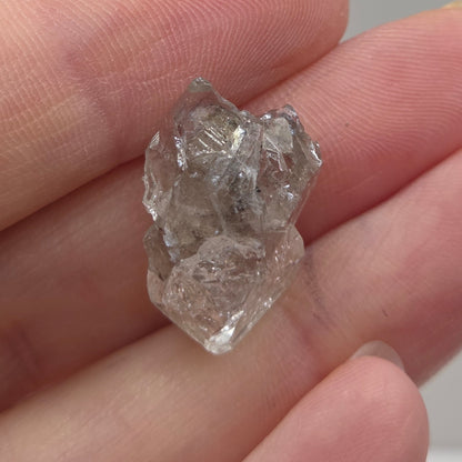 Raw diamond held between fingers against a neutral background