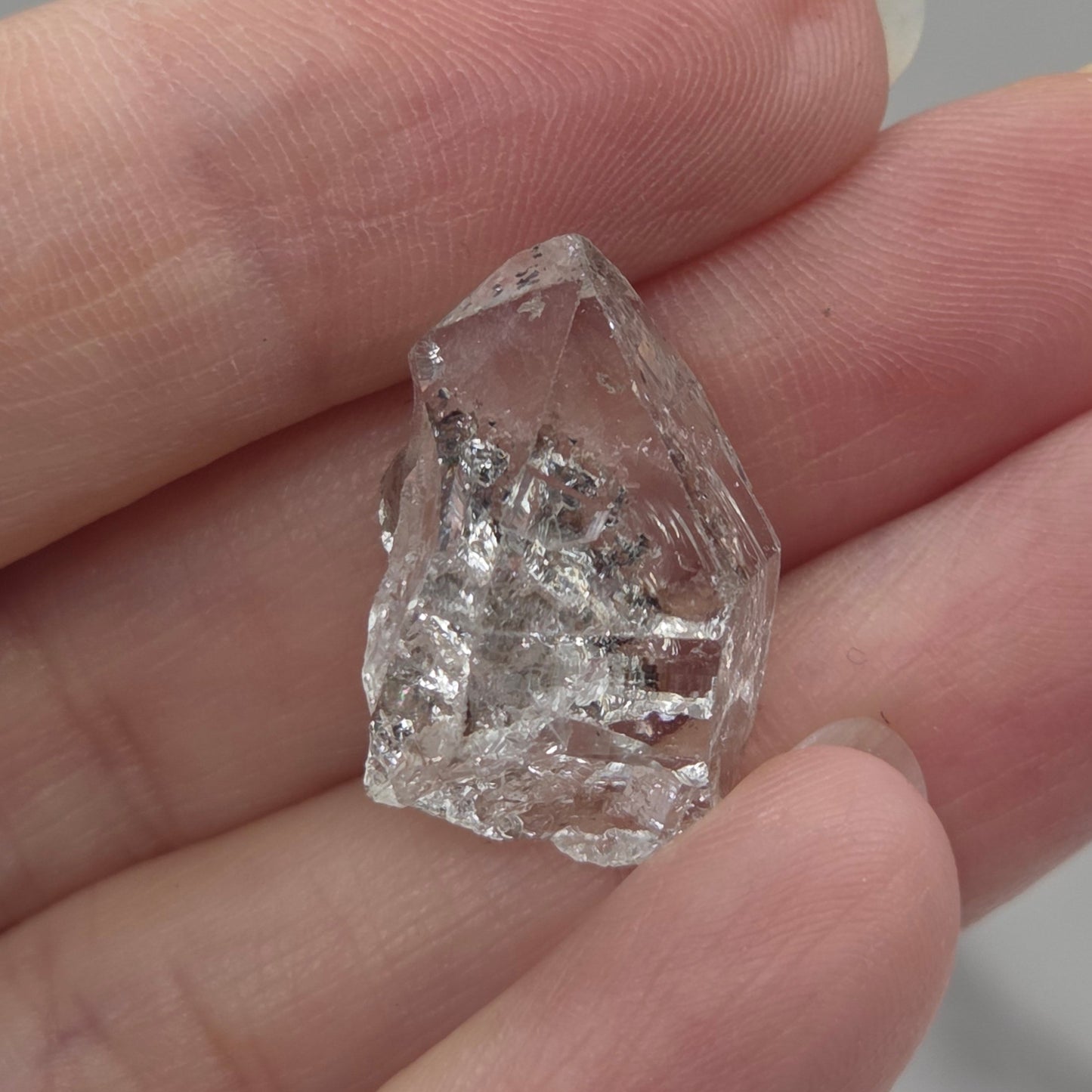 Raw diamond held between fingers against a neutral background