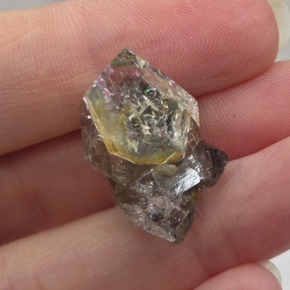 Hand holding a rough diamond crystal against a neutral background