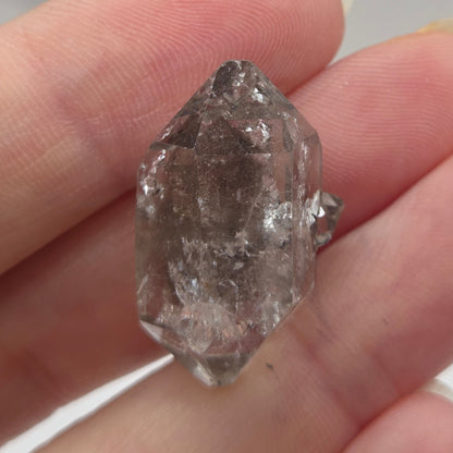 Raw diamond held between fingers against a neutral background