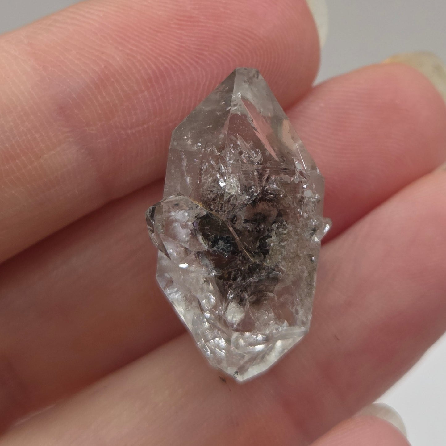 Clear crystal held between fingers against a neutral background
