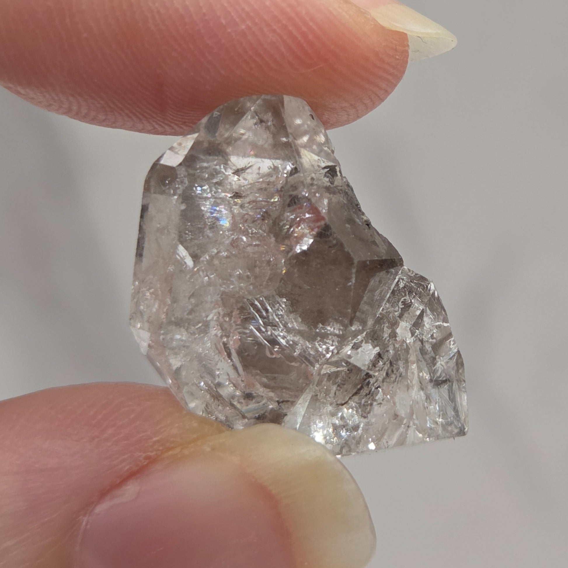 Raw diamond held between two fingers against a neutral background