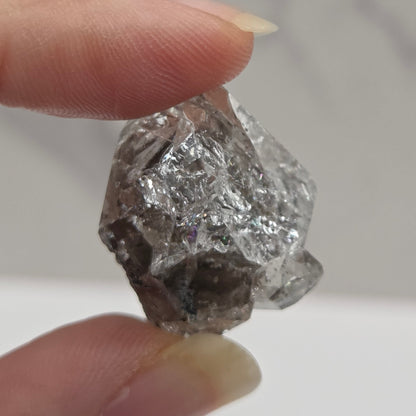 Raw diamond held between two fingers against a neutral background