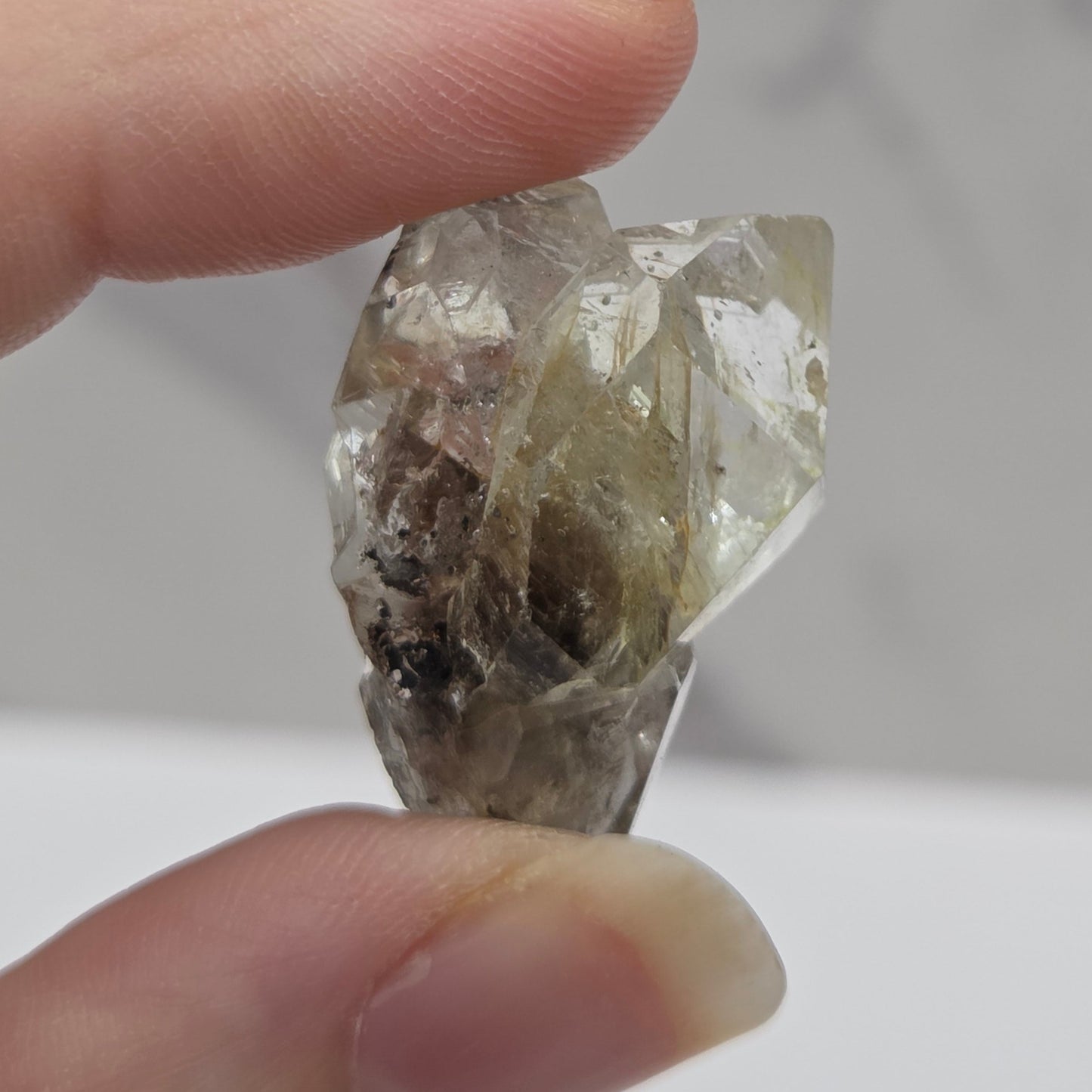 Hand holding a rough diamond crystal against a neutral background