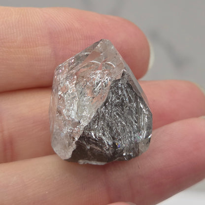 Raw diamond held in a hand against a neutral background