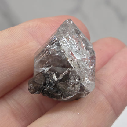 Raw diamond held between fingers against a neutral background