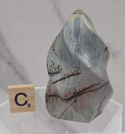 Picture Jasper carving resembling a flame on a clear stand against a neutral background