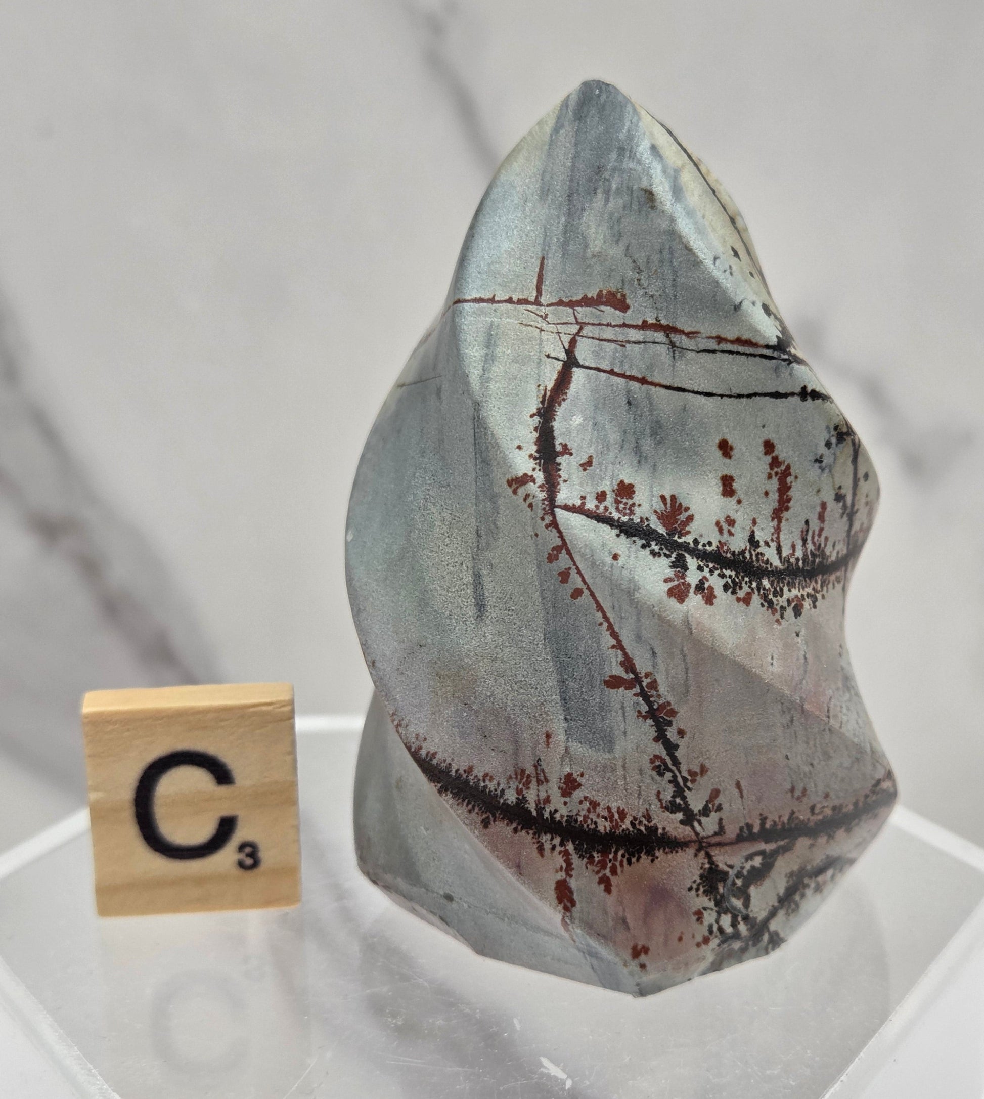 Picture Jasper carving resembling a flame on a clear stand against a neutral background