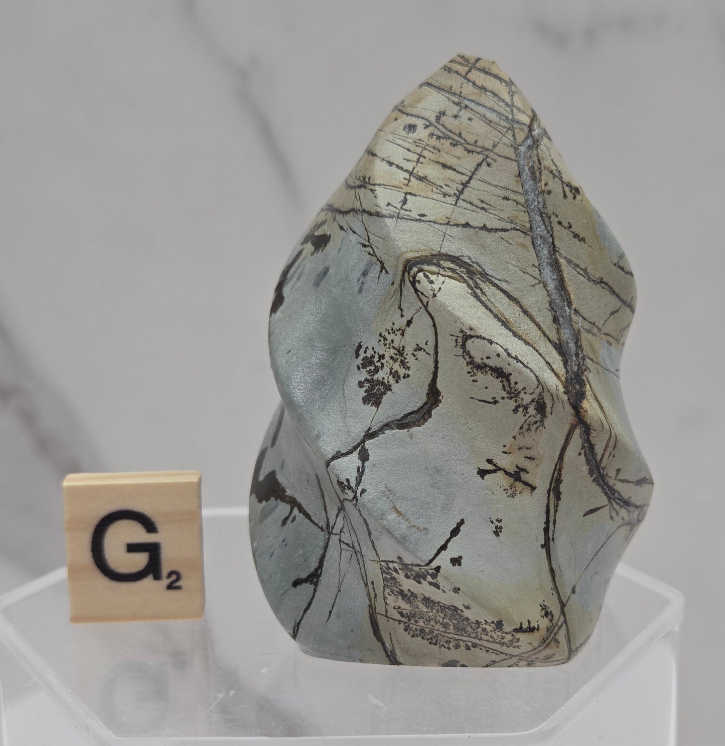 Picture Jasper carving resembling a flame on a clear stand against a neutral background