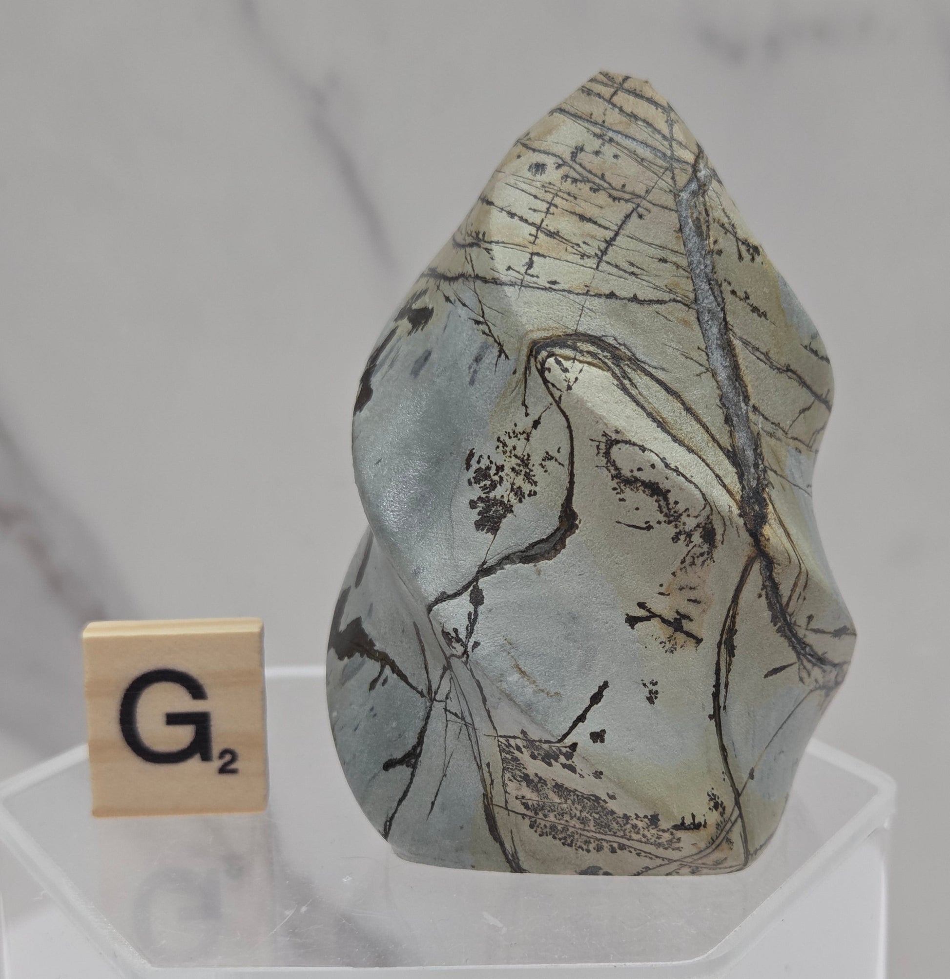 Picture Jasper carving resembling a flame on a clear stand against a neutral background