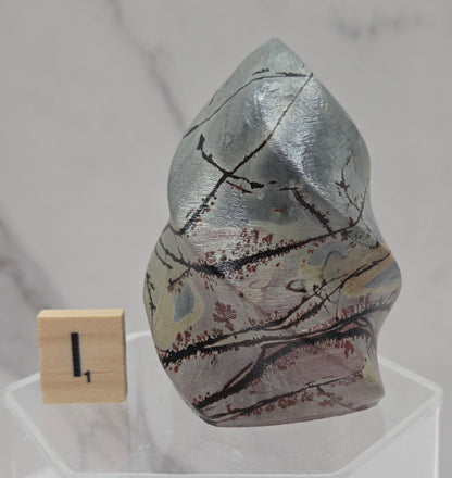Picture Jasper carving resembling a flame on a clear stand against a neutral background
