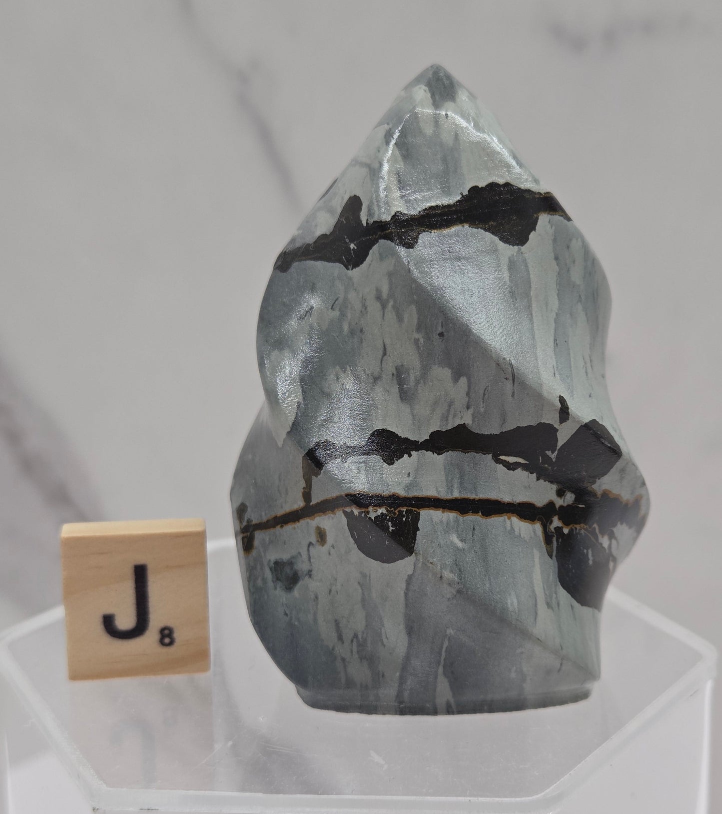 Picture Jasper carving resembling a flame on a clear stand against a neutral background