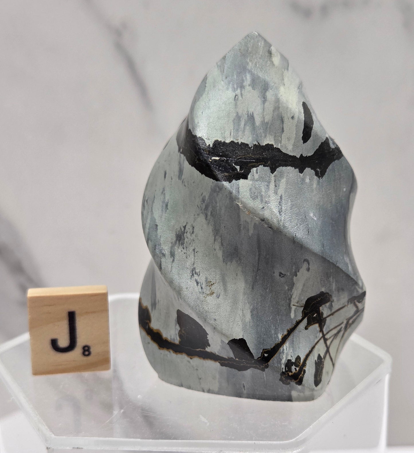 Picture Jasper carving resembling a flame on a clear stand against a neutral background