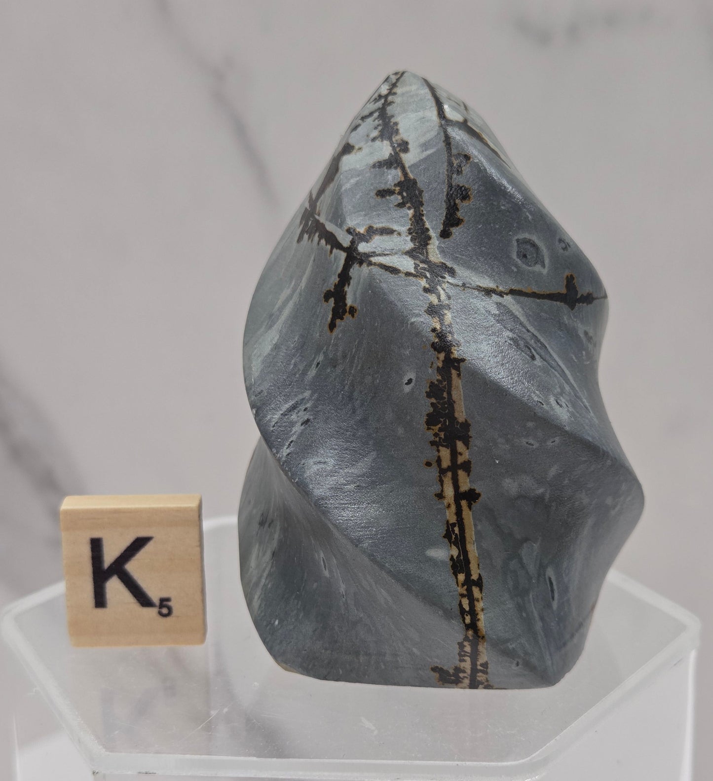 Picture Jasper carving resembling a flame on a clear stand against a neutral background