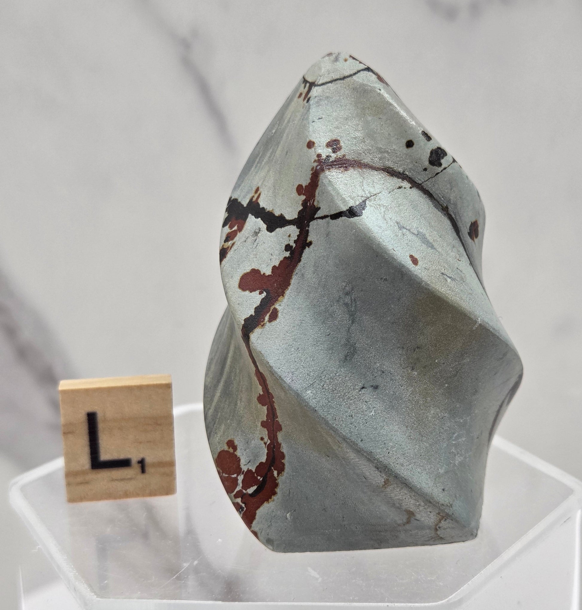 Picture Jasper carving resembling a flame on a clear stand against a neutral background