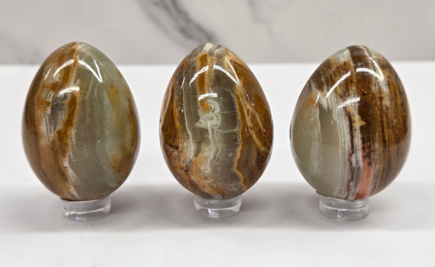 3 afghan jade egg carvings with green and brown bands against a neutral background