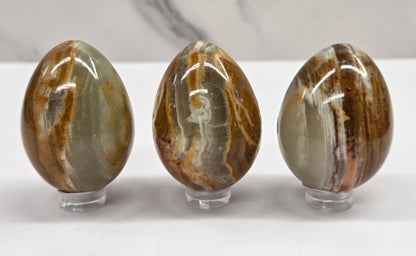 3 afghan jade egg carvings with green and brown bands against a neutral background
