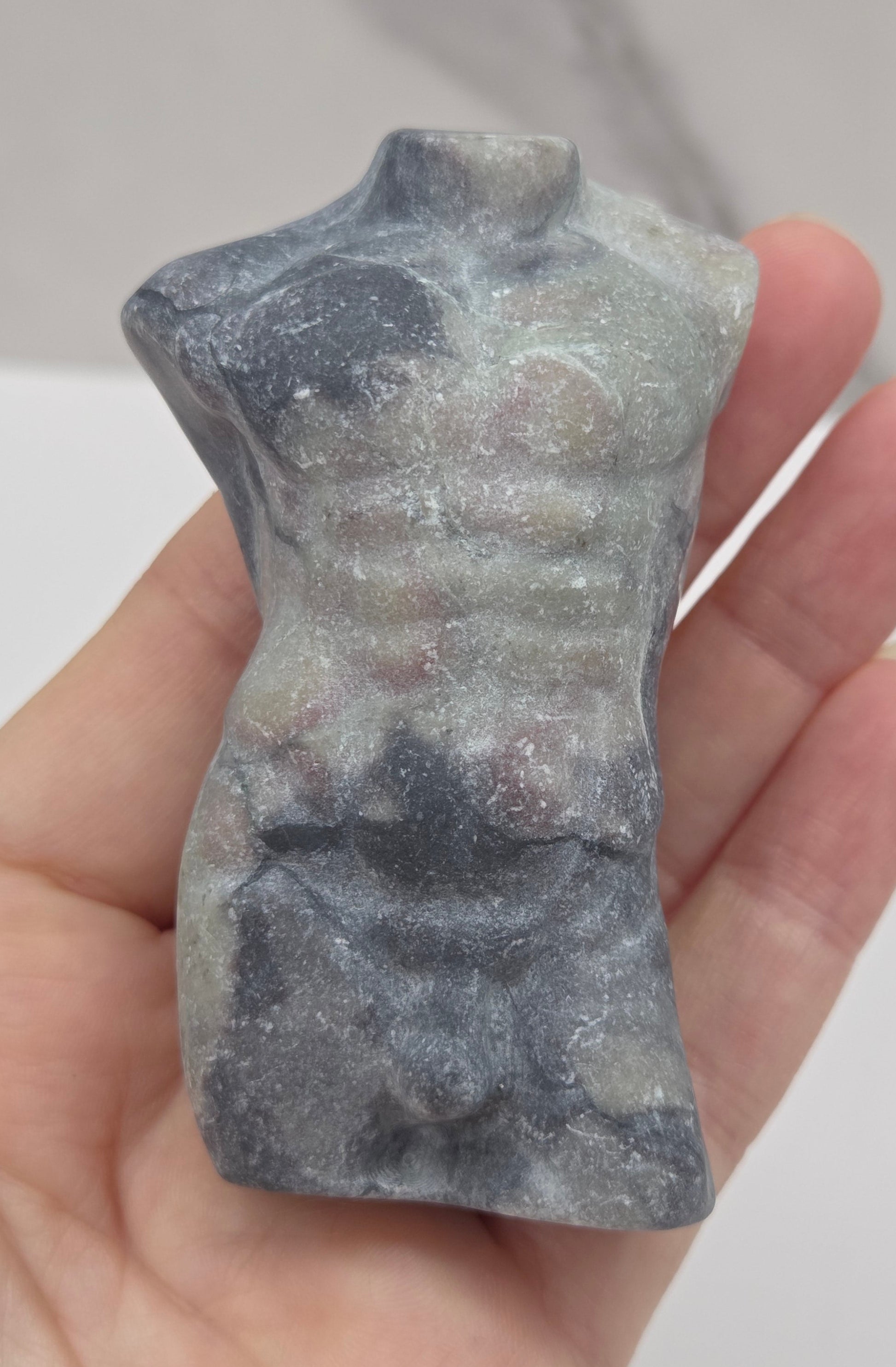 Hand holding a jasper male torso carving against a white background