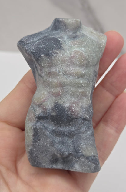 Hand holding a jasper male torso carving against a white background