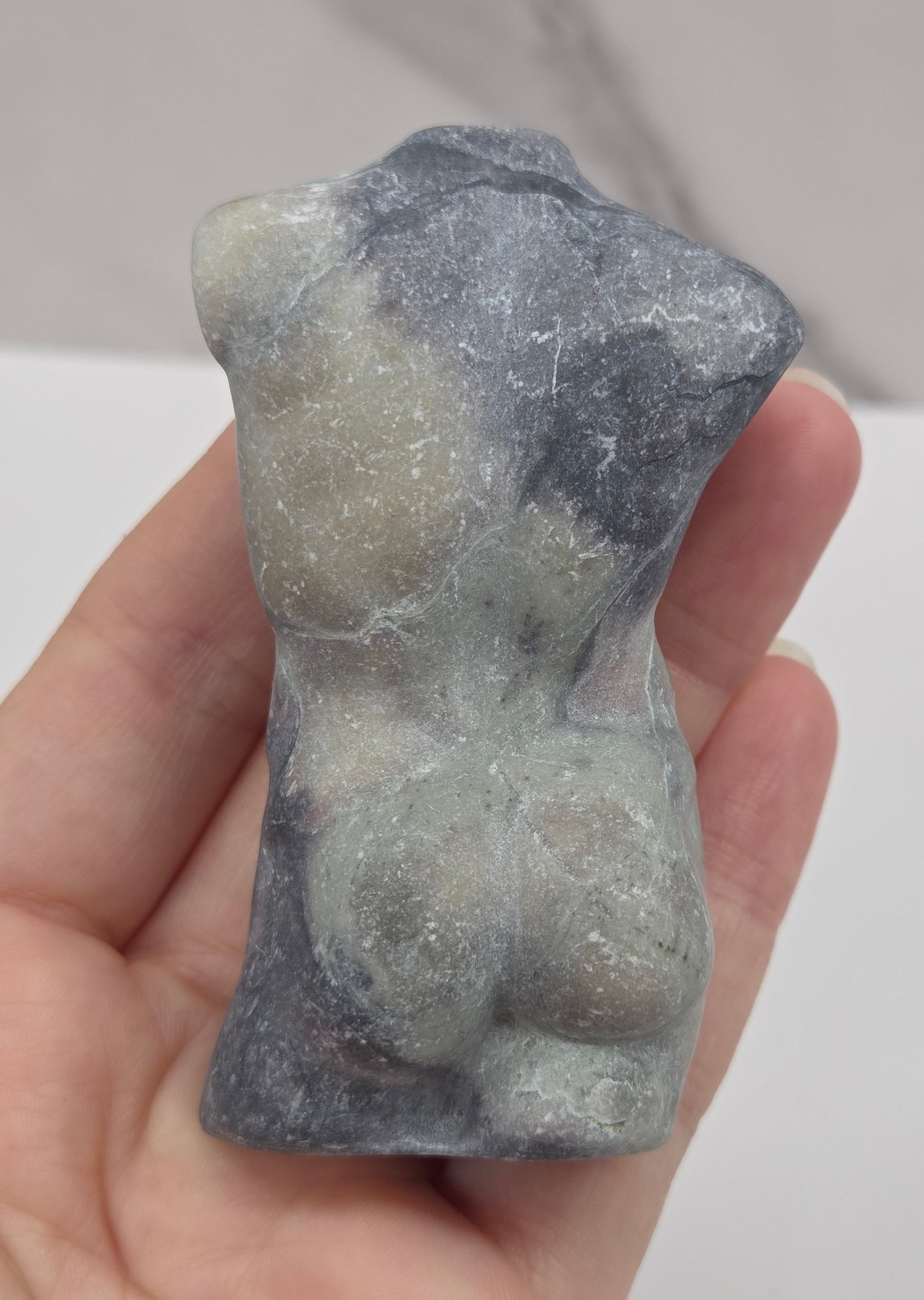 Hand holding a jasper male torso carving against a white background