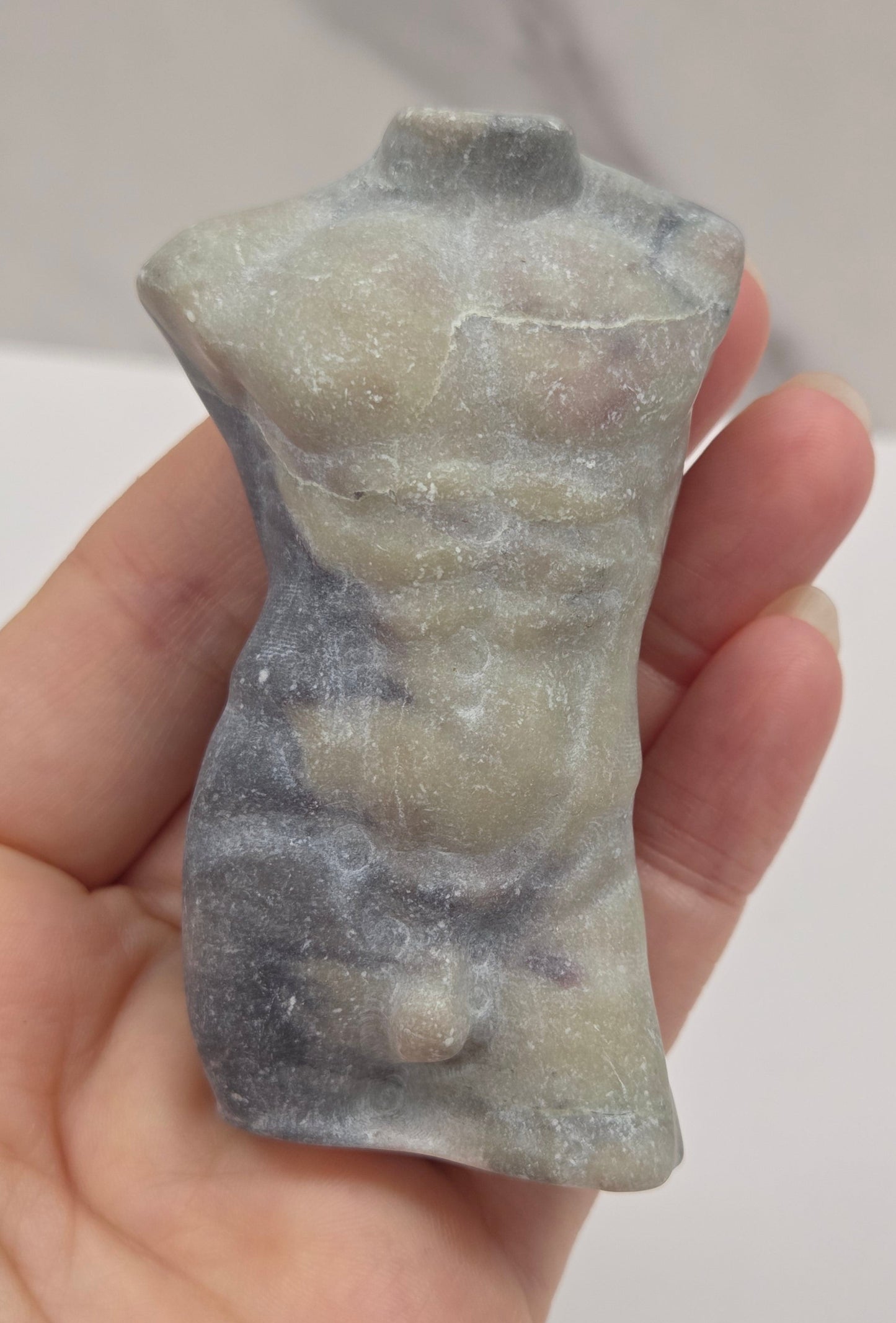 Hand holding a jasper male torso carving against a white background