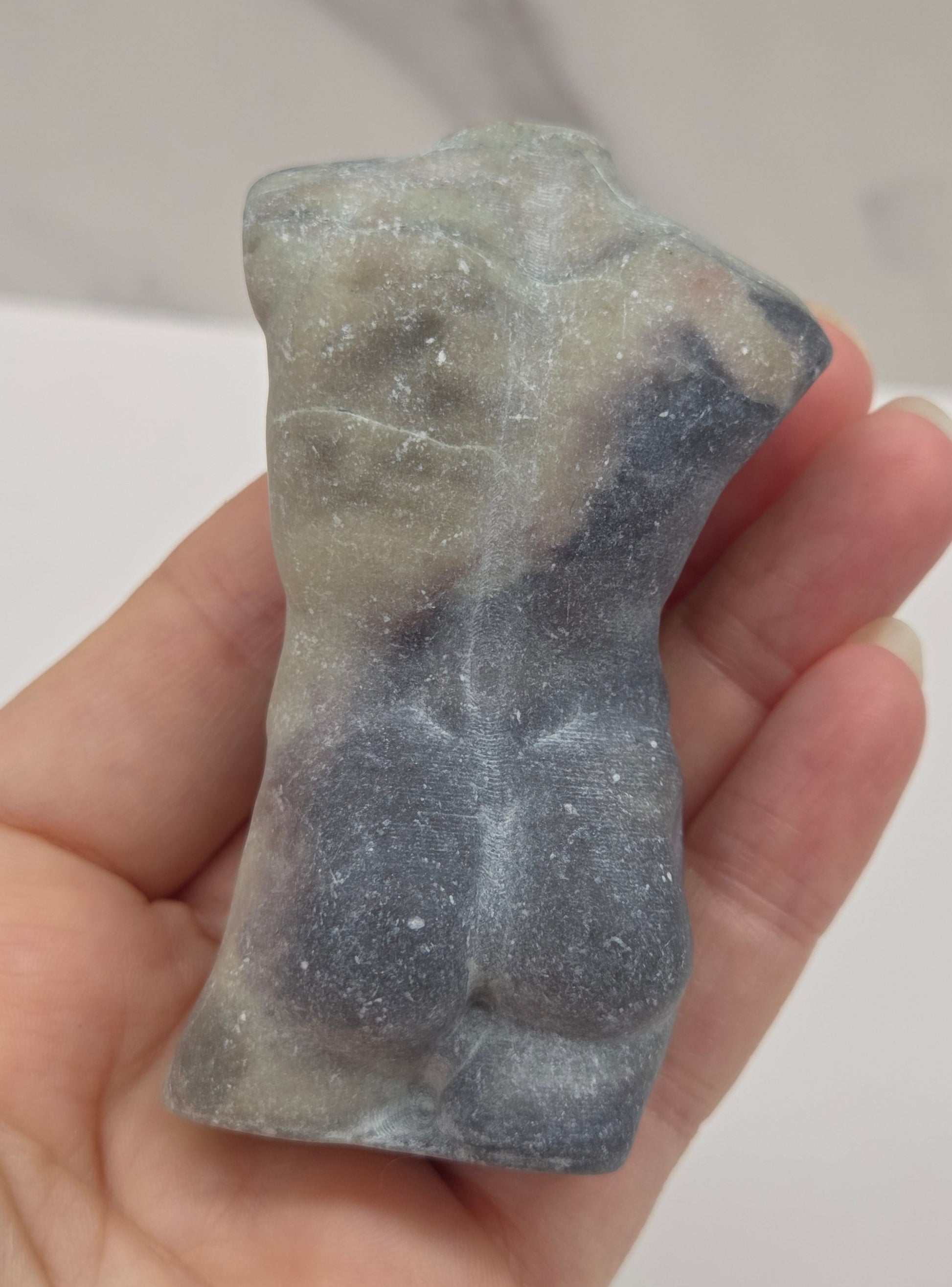 Hand holding a jasper male torso carving against a white background
