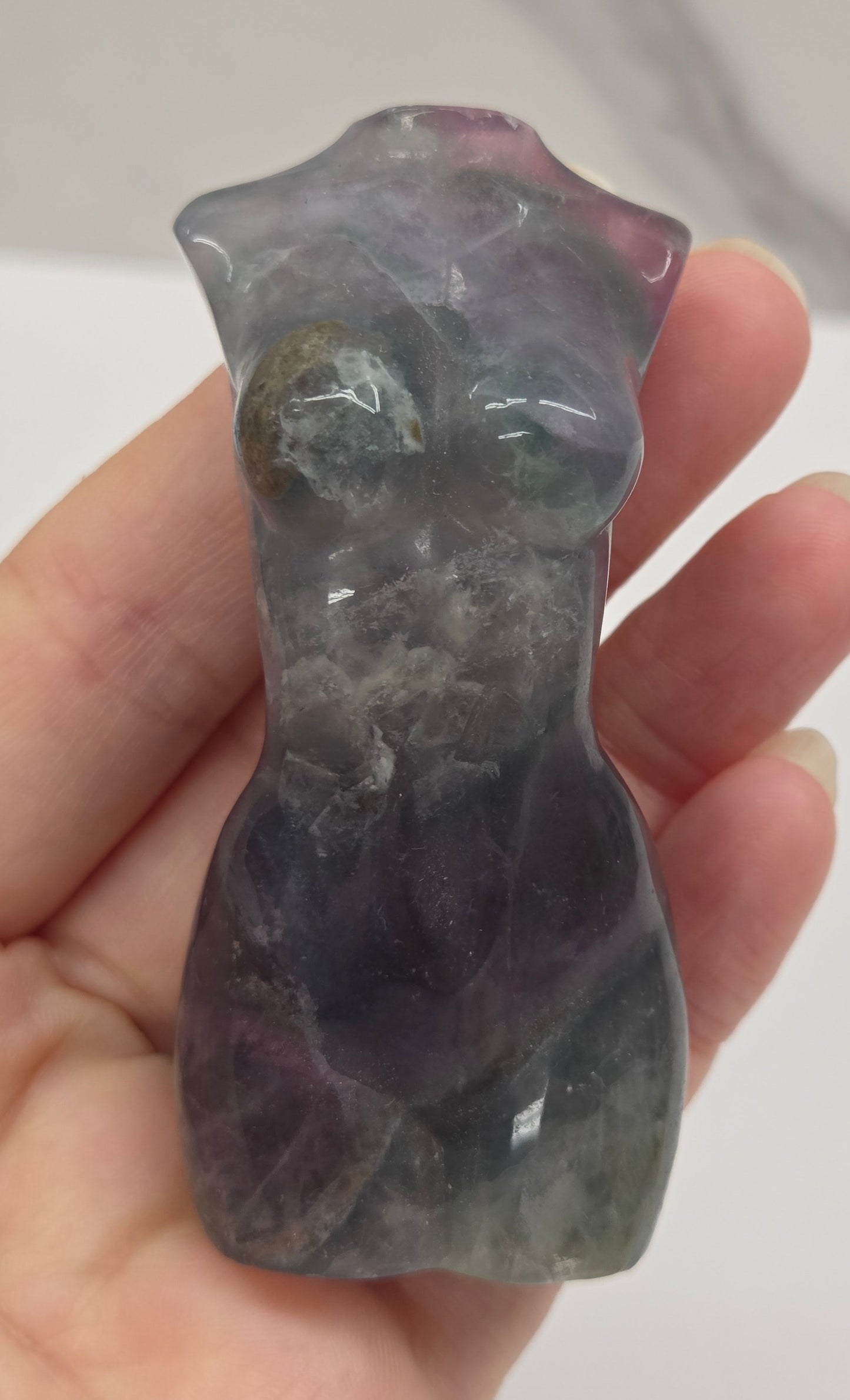 Female torso carving made of fluorite being held in a hand on a white background