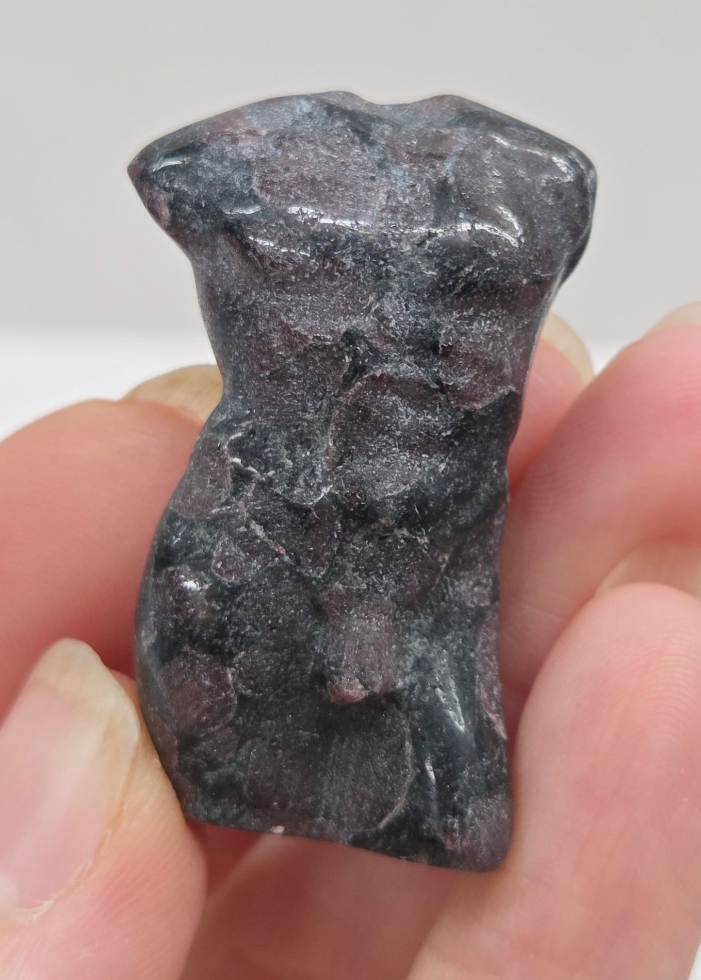 Hand holding a male torso crystal carving against a white background