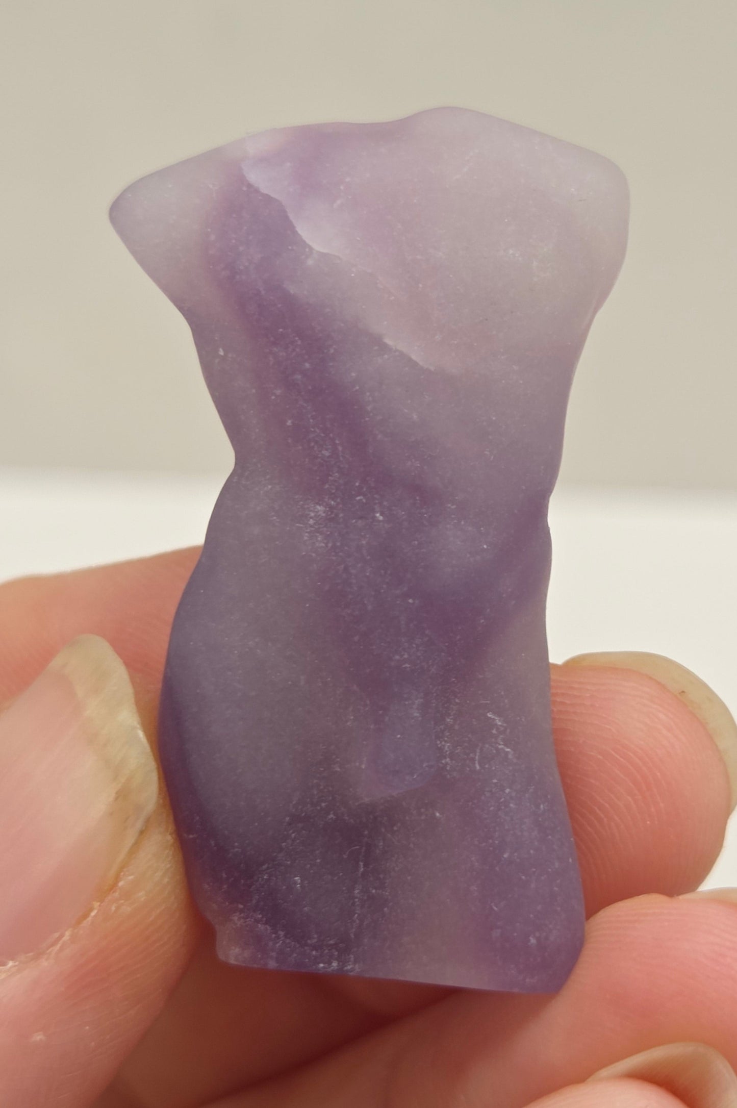 Hand holding a male torso crystal carving against a white background