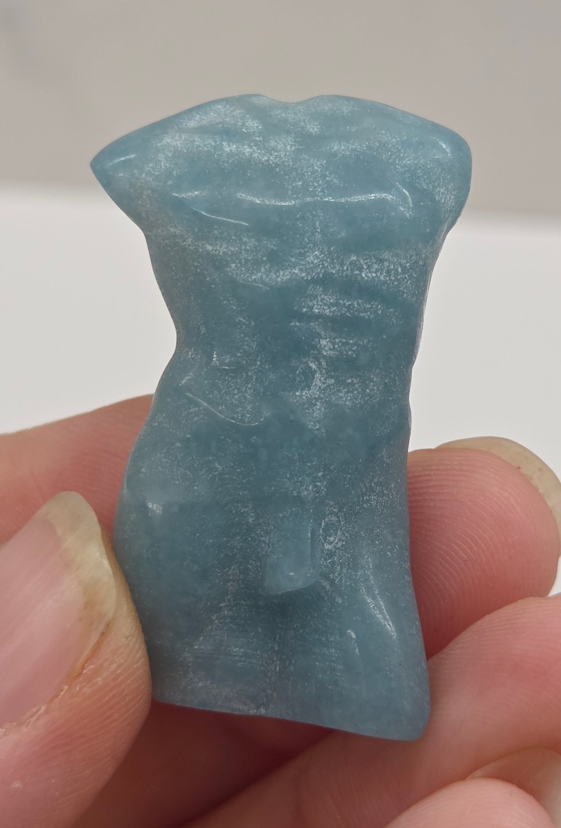 Hand holding a male torso crystal carving against a white background