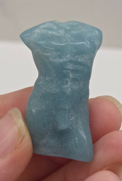 Hand holding a male torso crystal carving against a white background