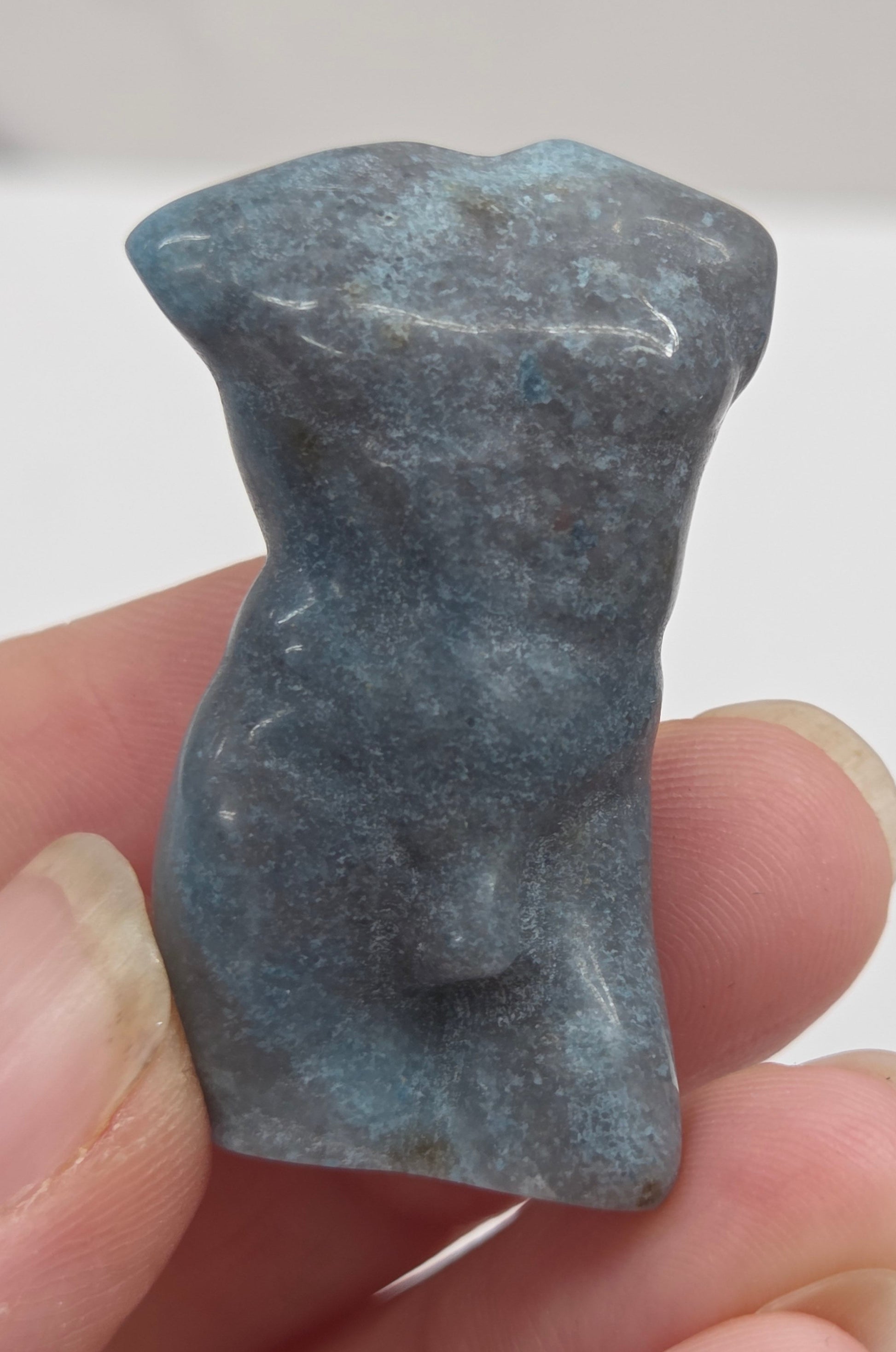 Hand holding a male torso crystal carving against a white background