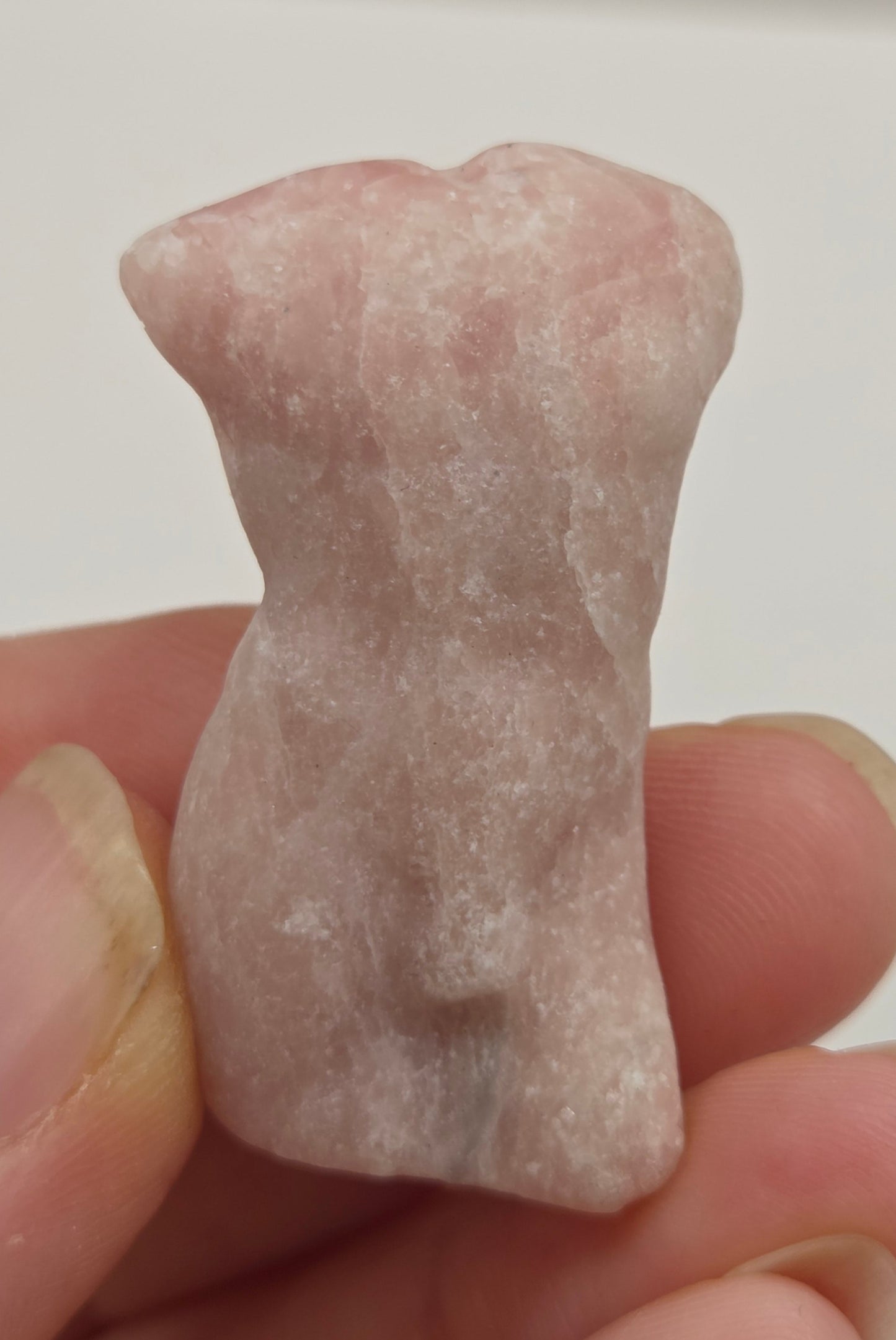 Hand holding a male torso crystal carving against a white background