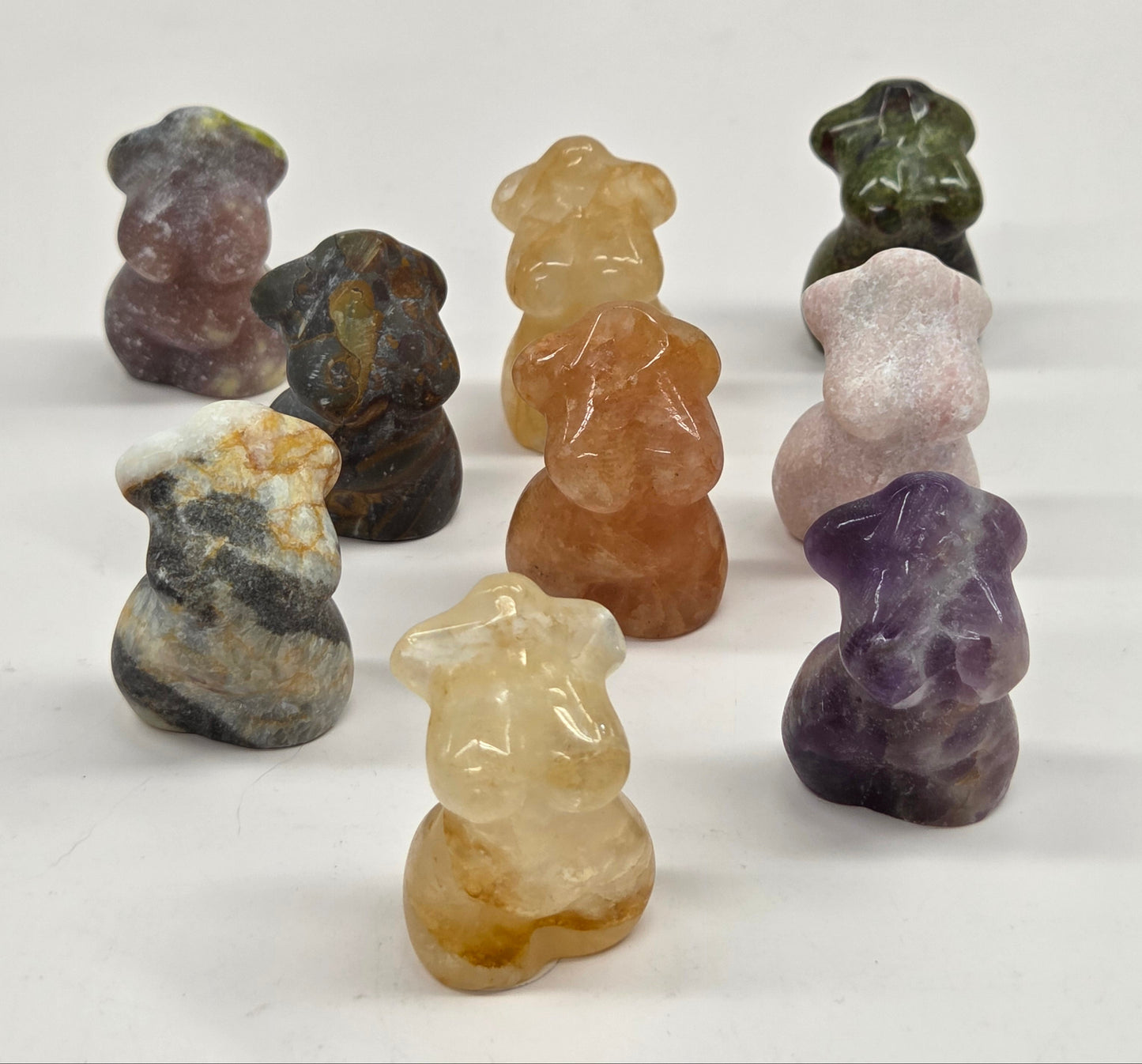 Collection of small female torso carvings made of a variety of materials and colors on a white background