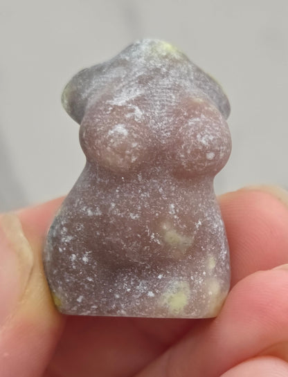 Hand holding a small crystal carving of a female torso against a white background