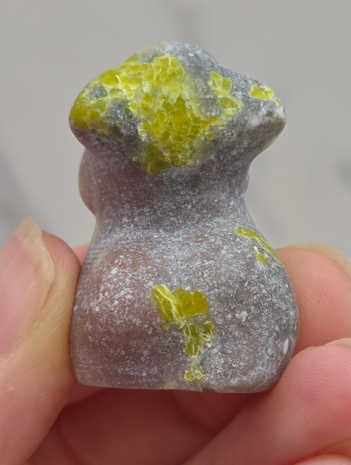 Hand holding a small crystal carving of a female torso against a white background