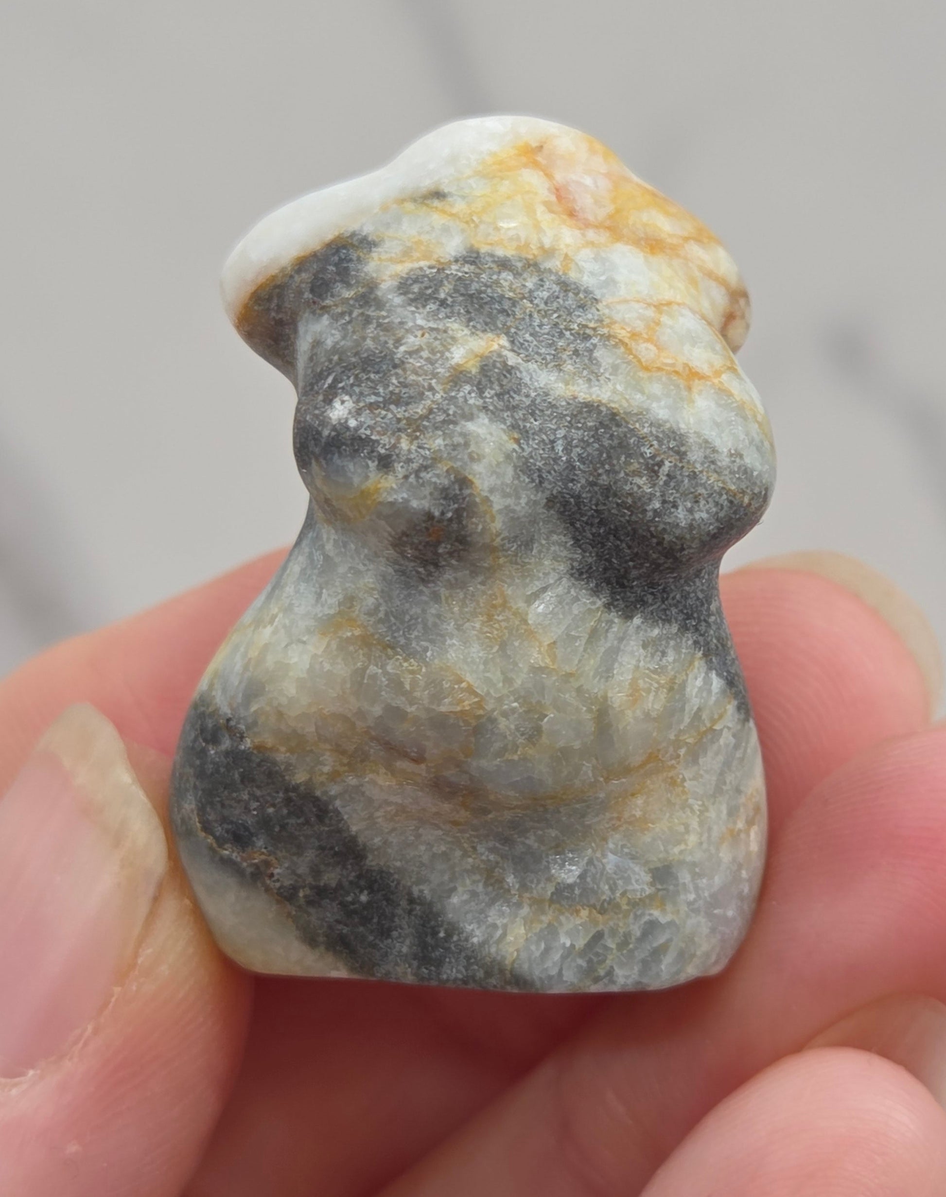 Hand holding a small crystal carving of a female torso against a white background