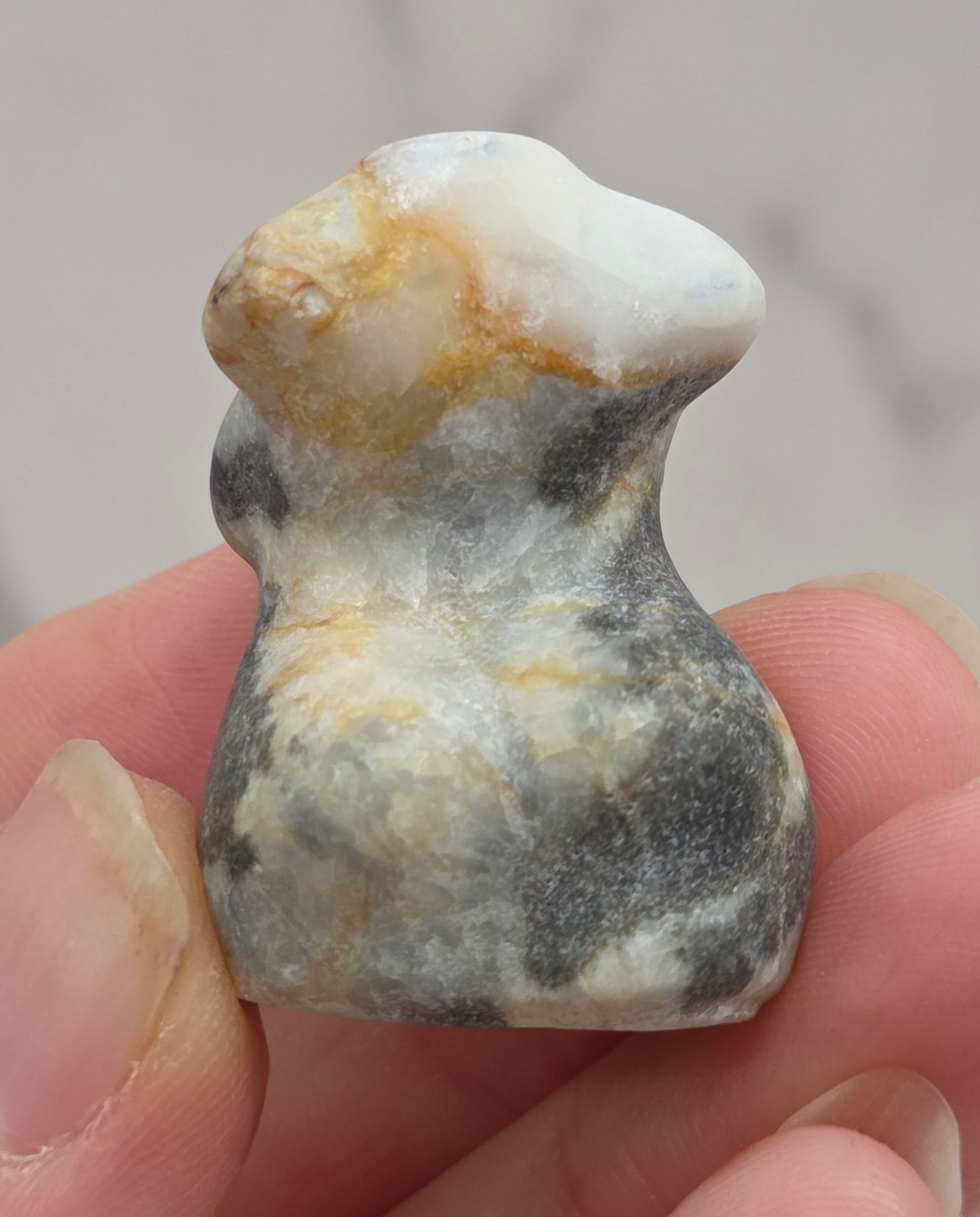 Hand holding a small crystal carving of a female torso against a white background