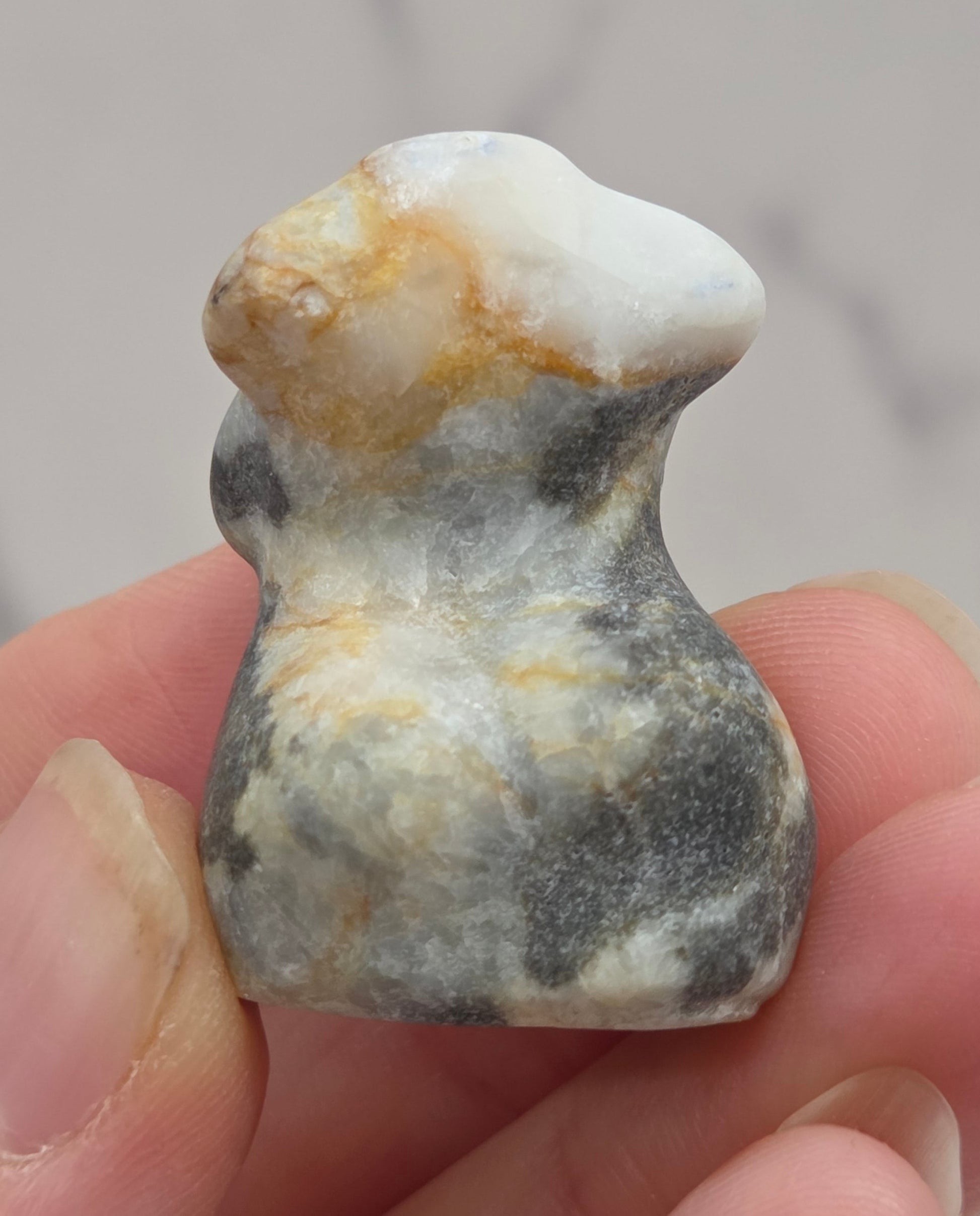Hand holding a small crystal carving of a female torso against a white background