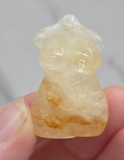 Hand holding a small crystal carving of a female torso against a white background