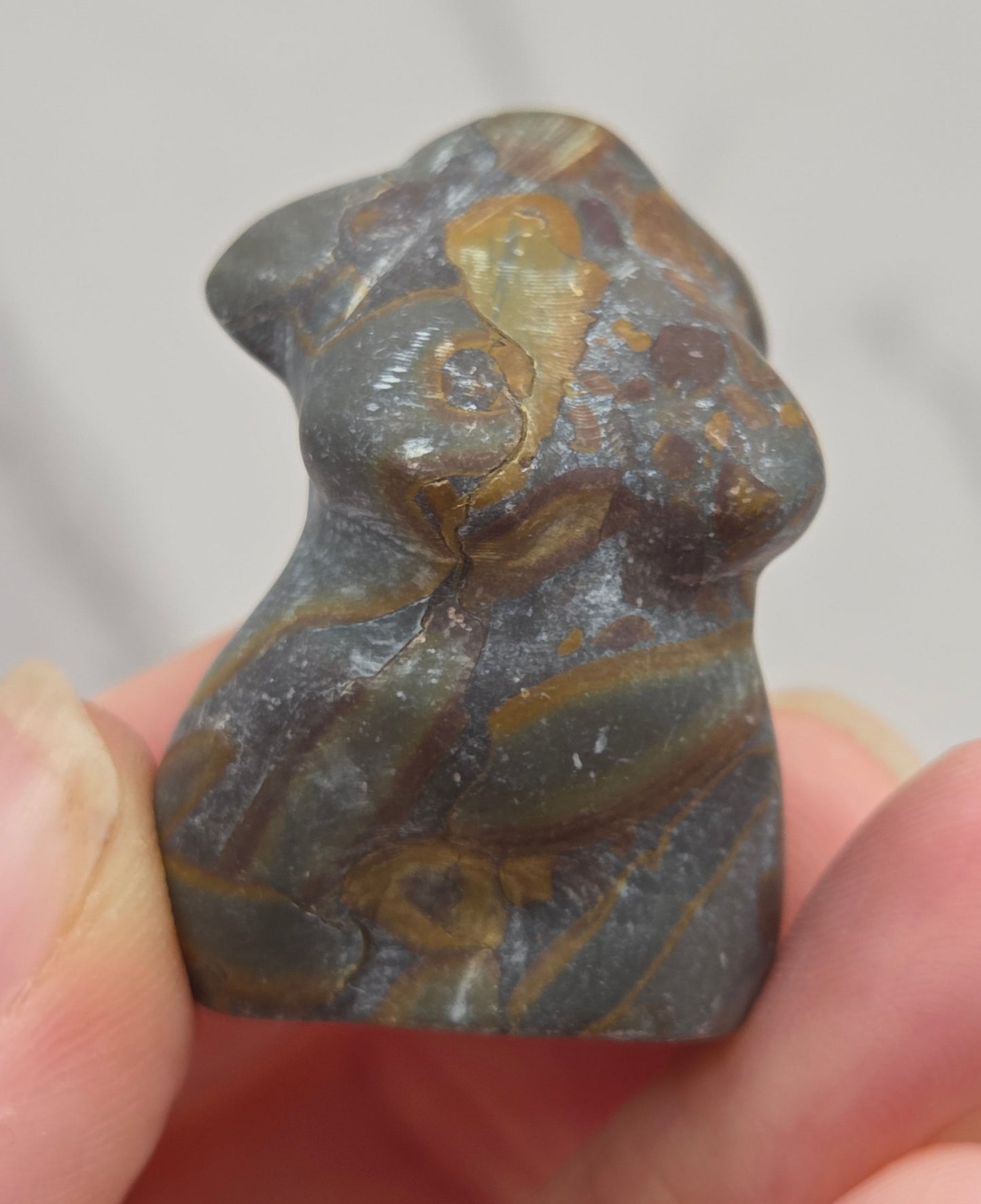 Hand holding a small crystal carving of a female torso against a white background